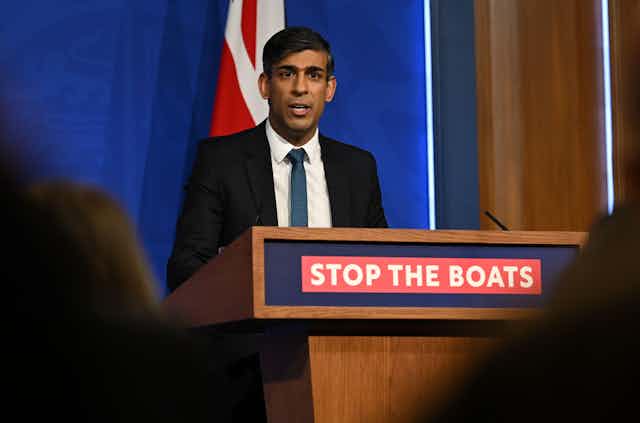 Rishi Sunak speaking at a podium that reads 'stop the boats'