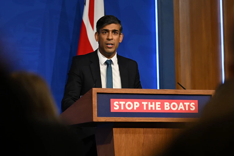 Rishi Sunak speaking at a podium that reads 'stop the boats'