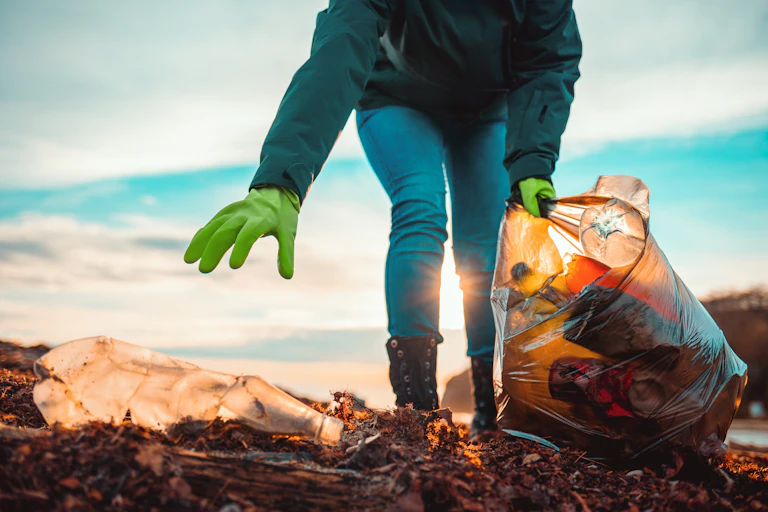A volunteer collects garbage on a muddy beach.