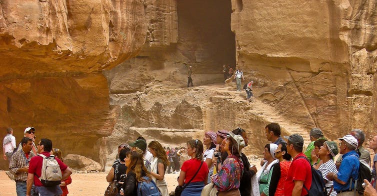 Un grupo de personas observa algo fuera del encuadre ante las murallas de una ciudad antigua.