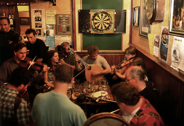 A group of traditional folk musicians gathered round playing in a Scottish pub.