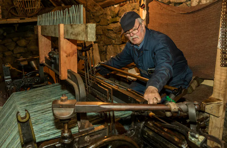 A man working an old-fashioned hand weaving loom.