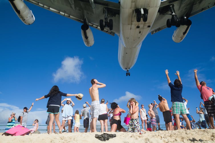 People on beach look at low flying plane