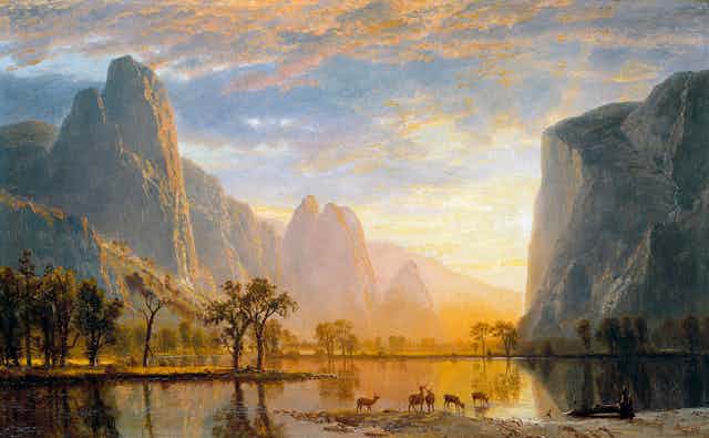 A painting of a lake surrounded by cliffs at sunset, with deer gazing off into the light.