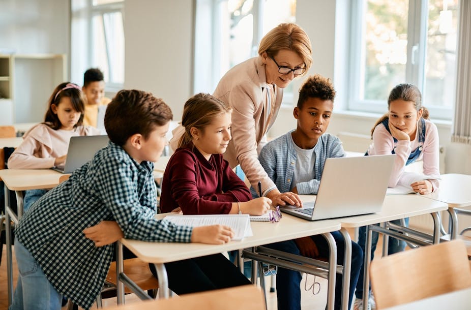 Des élèves et leur enseignante regardent un ordinateur