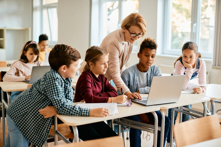 Des élèves et leur enseignante regardent un ordinateur