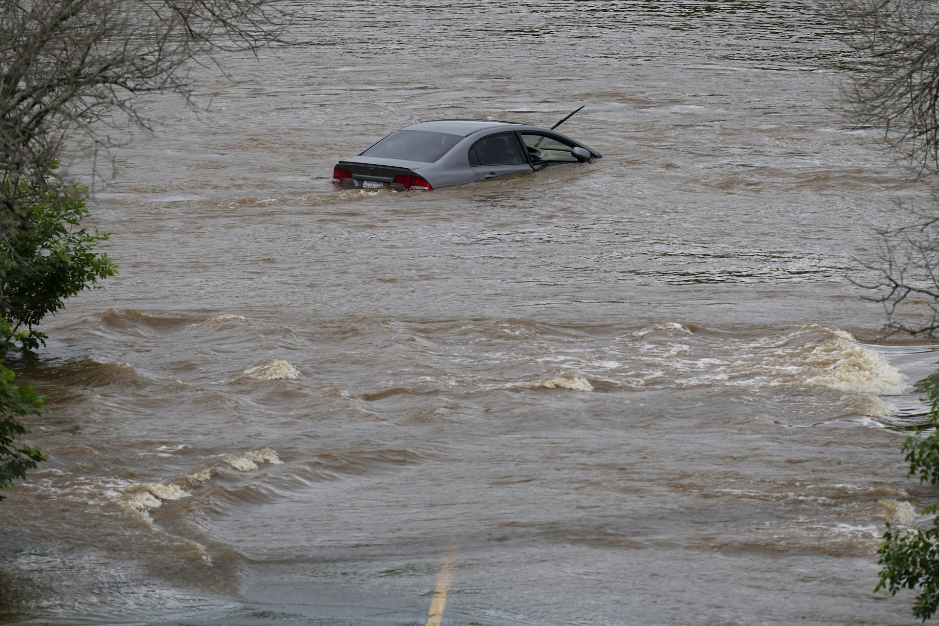 A car is almost fully submerged in a flooded parking lot.