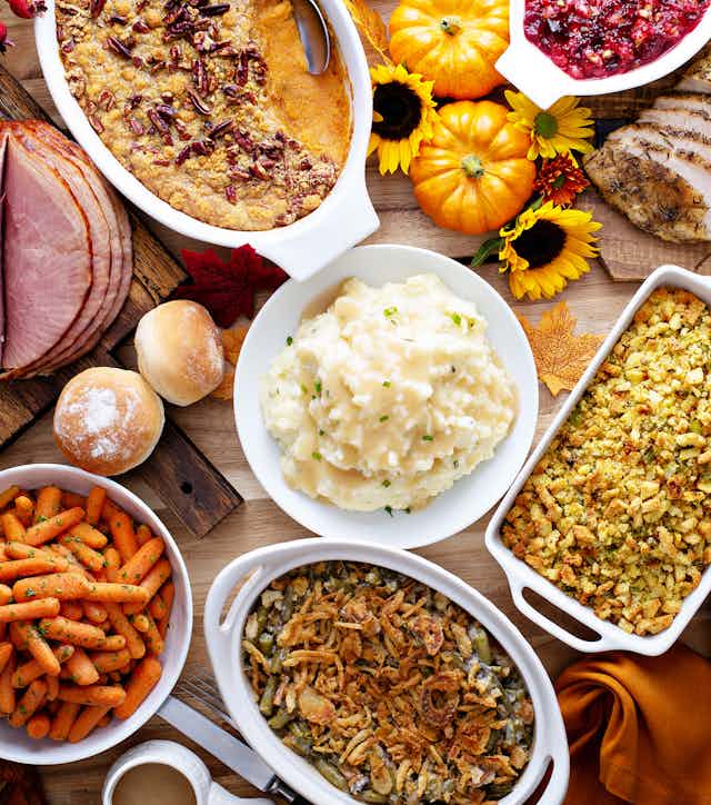 A bird's eye view of a Thanksgiving table with roasted turkey, sliced ham, baby carrots, greens, mashed potatoes, gravy, rolls, sweet potatoes and pie.