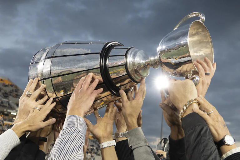 Multiple pairs of hands holding up a large silver sport trophy