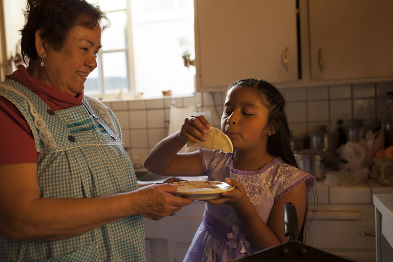 Hispanic woman cooking for granddaughter in kitchen
