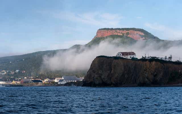 A row of buildings overlook the ocean against the backdrop of a cliff side.