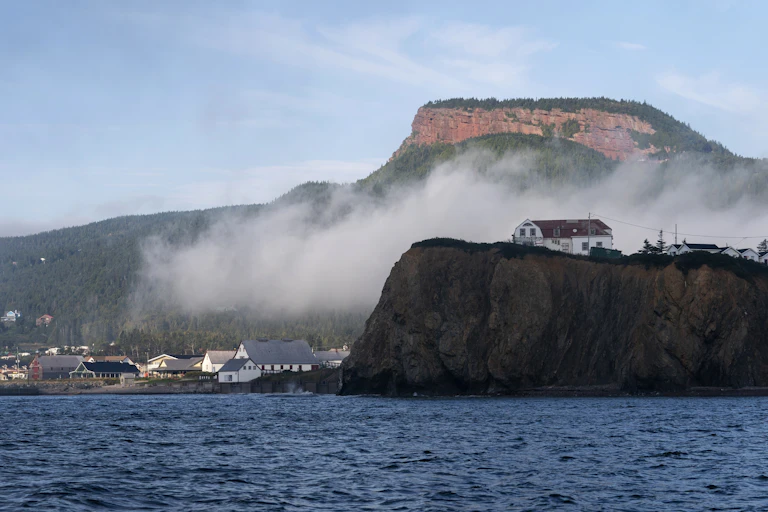 A row of buildings overlook the ocean against the backdrop of a cliff side.