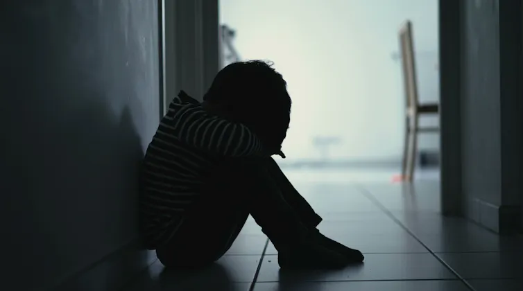 A small boy sits with his head in his knees