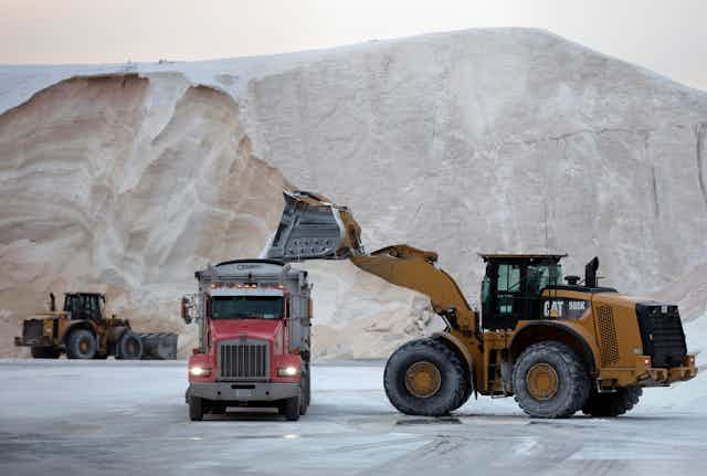 A massive mound of road salt is in the background as the loader fills a dump truck.