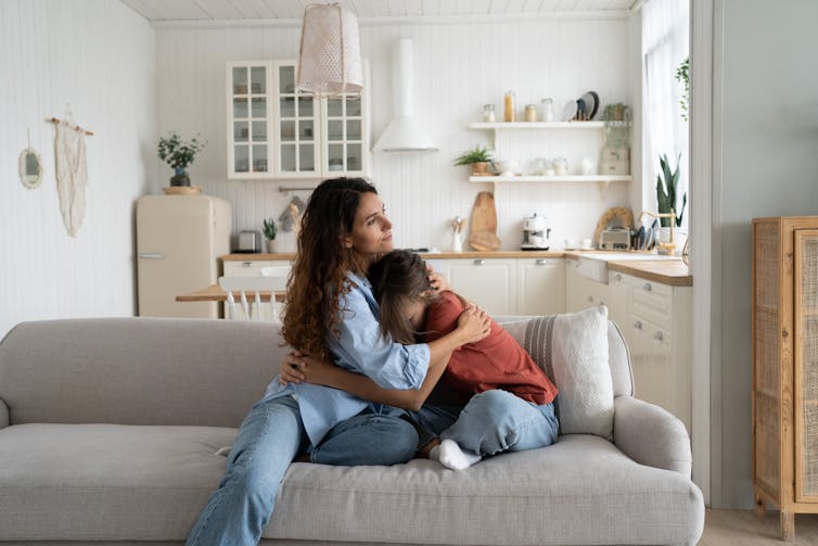 A woman on a couch hugs a small child.