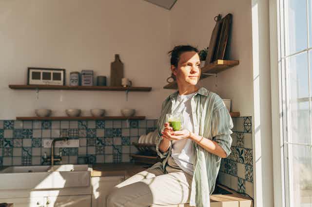 A woman in the kitchen holding a green drink.