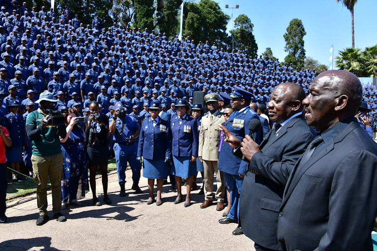 A man wearing a suit speaks into a mike held in his left hand before a crowd of policemen and women.