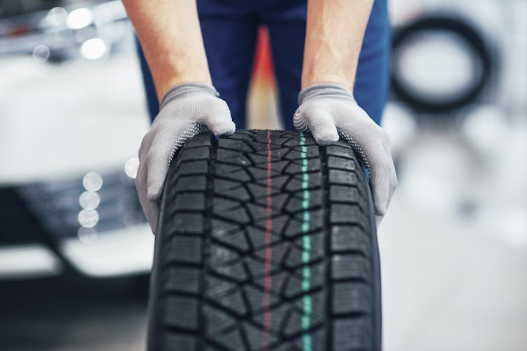 A mechanic pushing a black tyre in a workshop.