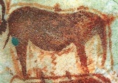 An image of an elephant drawn on the wall of a cave in vivid reds and oranges
