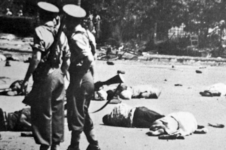 Two policemen walk among people lying dead on the ground.
