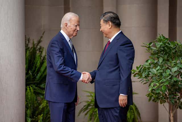 Two men wearing blue suits shake hands, Joe Biden and Xi Jinping.