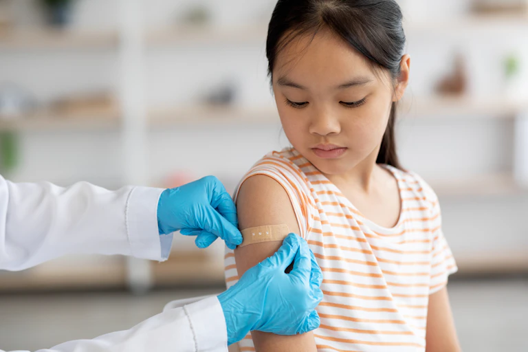 A doctor puts bandaid on a teenage girl's arm.