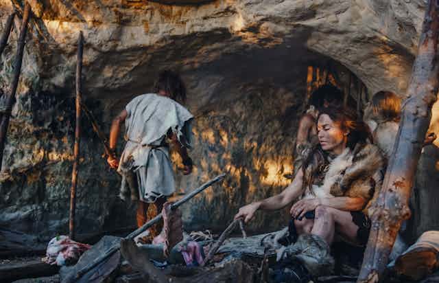 pessoas vestidas com peles do lado de fora de uma caverna, uma mulher sentada em uma fogueira
