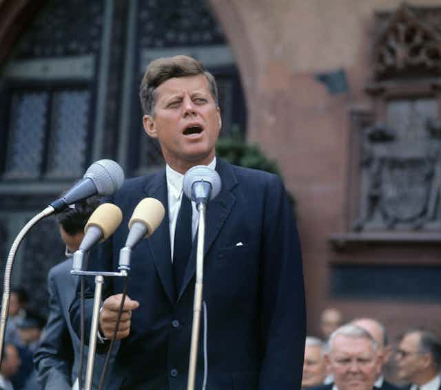 John F Kennedy standing in front of microphones.