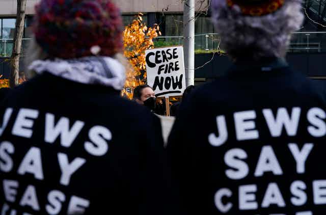 People wear shirts and hold signs saying 'cease fire now' and 'Jews say cease fire'