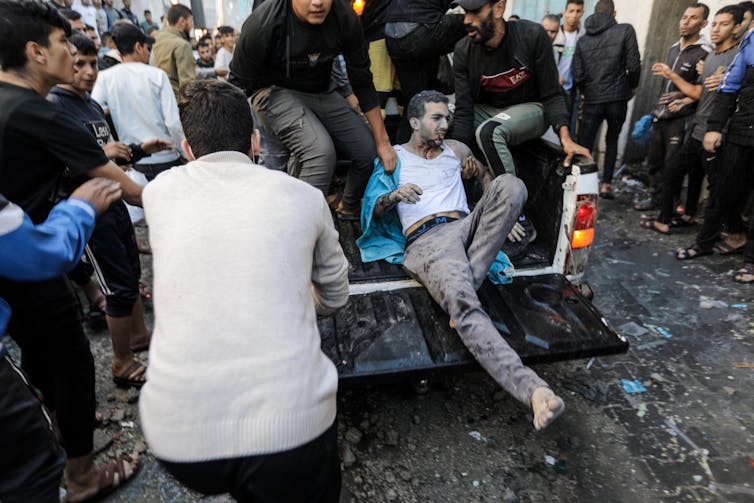 People help a dust-covered man into the back of a truck.