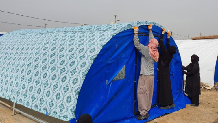 Three people cover a tent with decorative fabric
