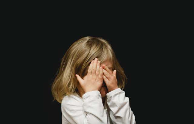 Une petite fille se cache le visage dans ses mains pendant qu’elle pleure