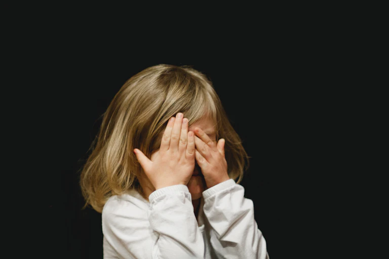 Une petite fille se cache le visage dans ses mains pendant qu’elle pleure