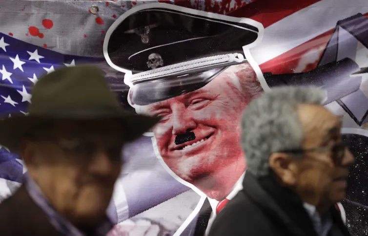 A banner of an older blond man with a Hitler moustache;.