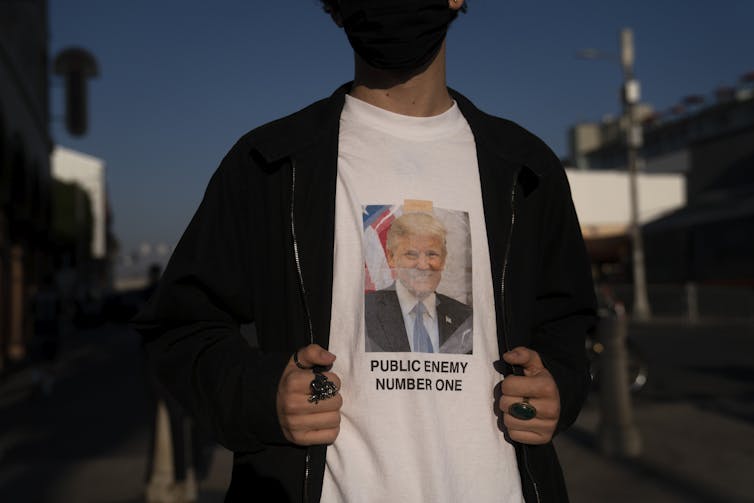 A person wears a T-shirt with Donald Trump's face that says Public Enemy Number One.