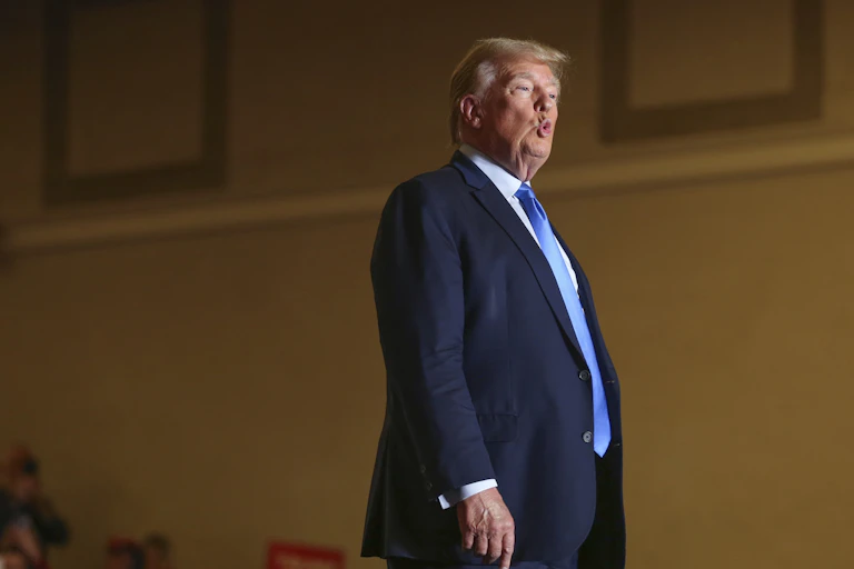 An older blond man stands with his lips pursed.