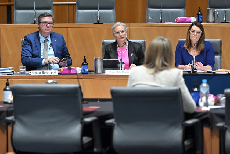 Woman sits alone in front of a panel of three people