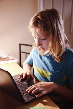 A young child sits at a desk, typing on a computer.