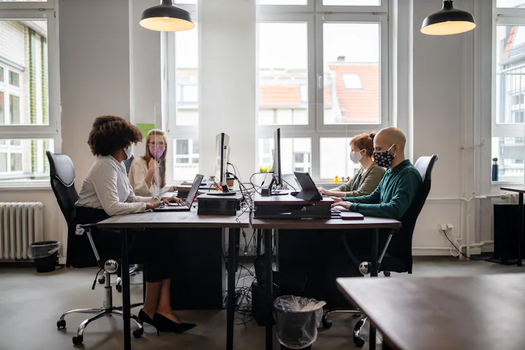 A group of people working in an office wearing masks.