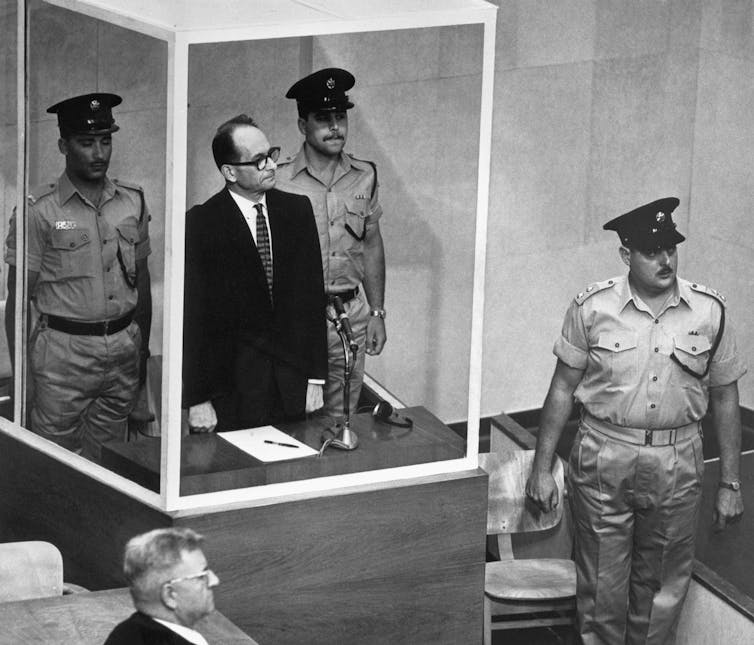A man stands in a bulletproof glass cage in court.