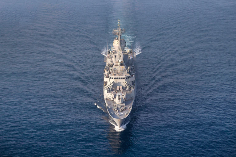A grey ship seen from a high angle as it approaches directly from the front