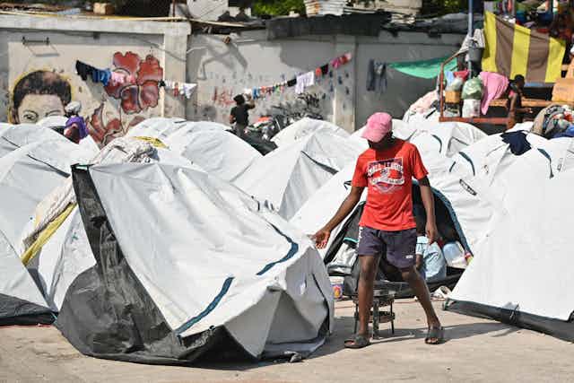 A man walking past several small white tents pitched on concrete ground