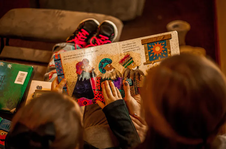 A silhueta de uma menina ao lado de uma adulta segurando e lendo juntas um livro ilustrado