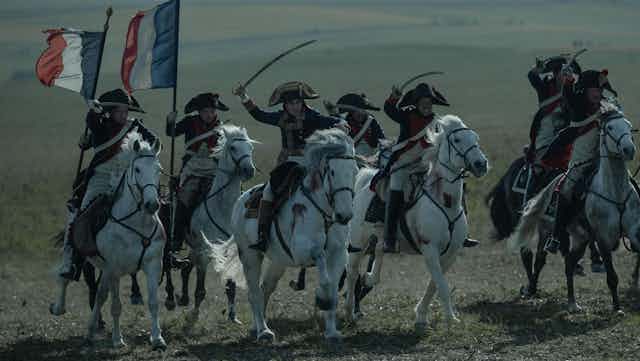 Escena de una película en la que un hombre a caballo con espada lidera a otros que le siguen y portan bandera francesa