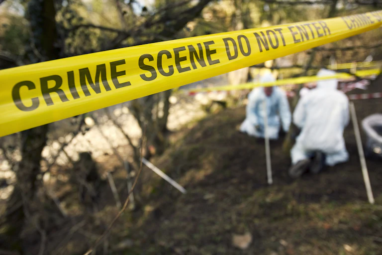 crime scene tape with PPE-wearing people kneeling on ground