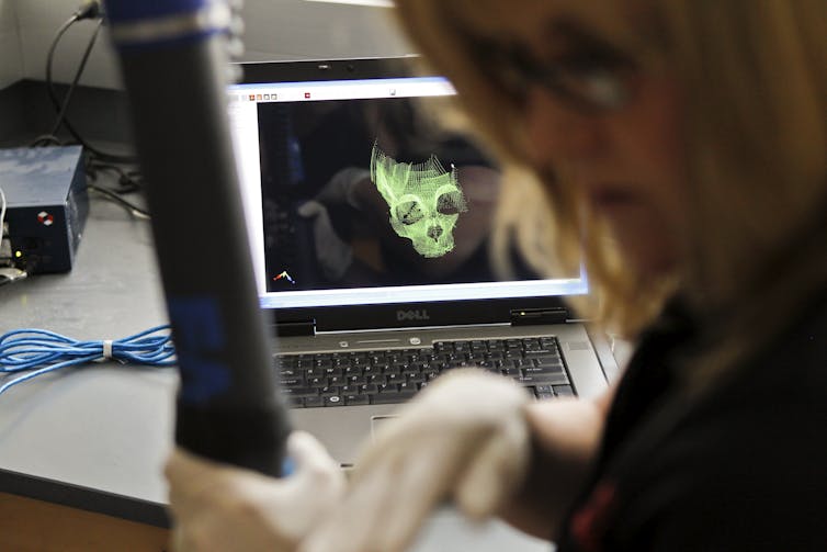 digital representation of a skull on a laptop screen with gloved woman in foreground