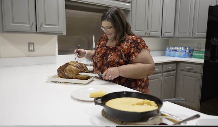 A woman stands in front of a cooked turkey that's sitting on a kitchen counter as she smiles and demonstrates how to handle poultry.