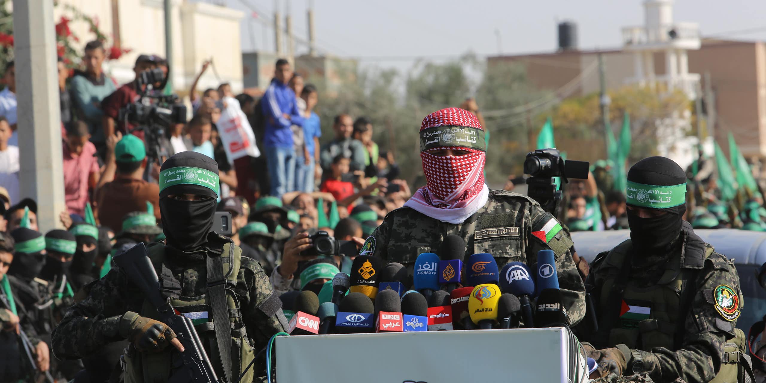 Des hommes masqués aux couleurs du Hamas prononcent un discours devant des micros. Derrière eux, des civils sont rassemblés.