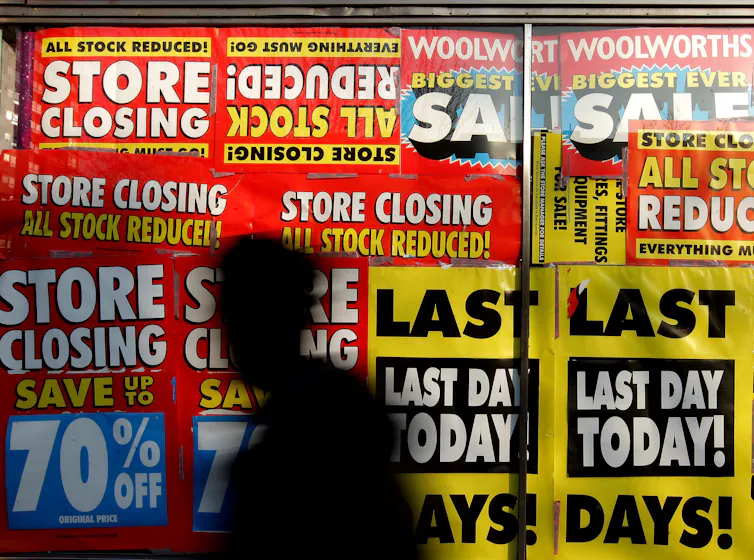 A silhouette of a person in front of a shop window plastered with closing-down signs.