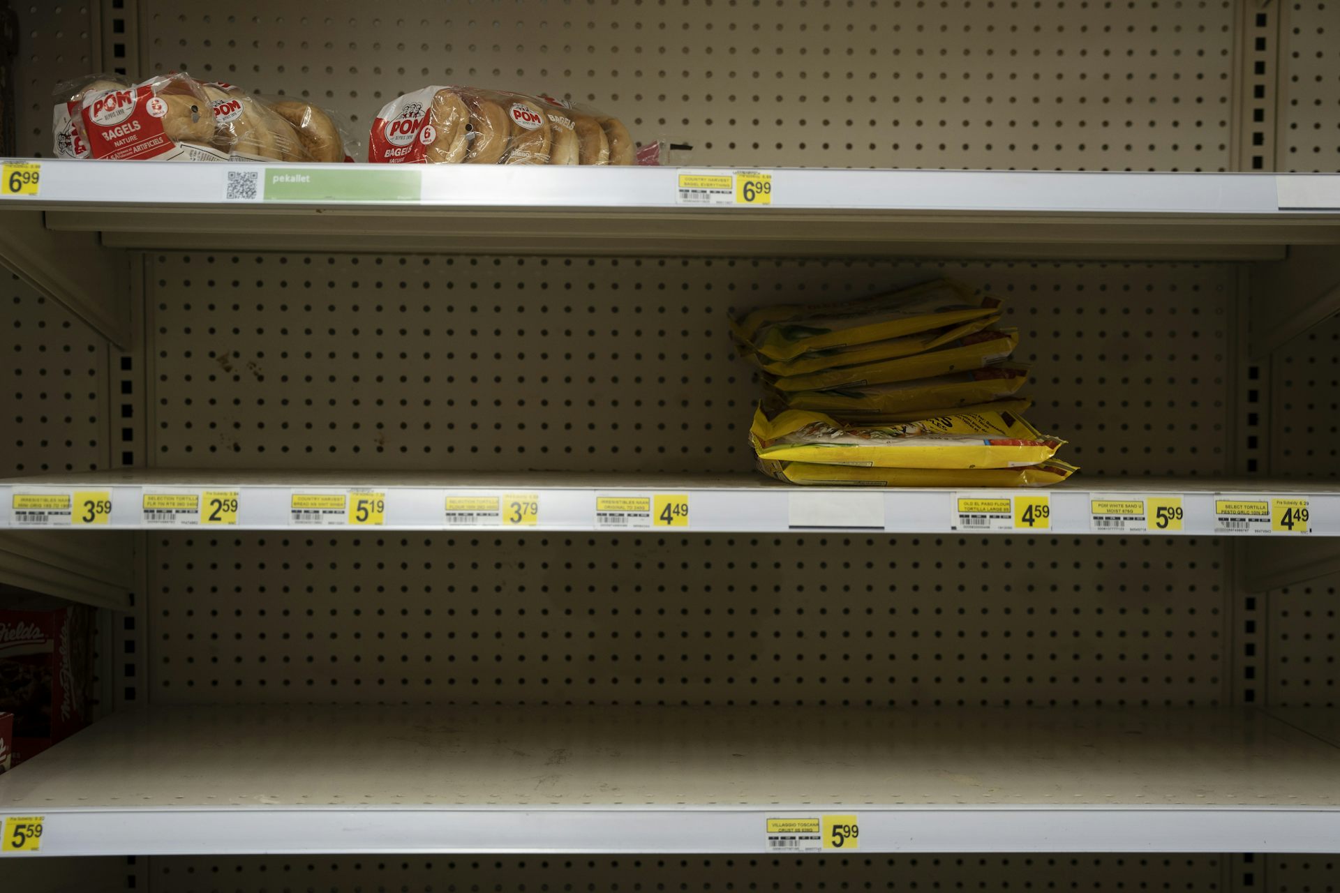 A scene of largely bare shelves in a store with only a few remaining items for purchase.